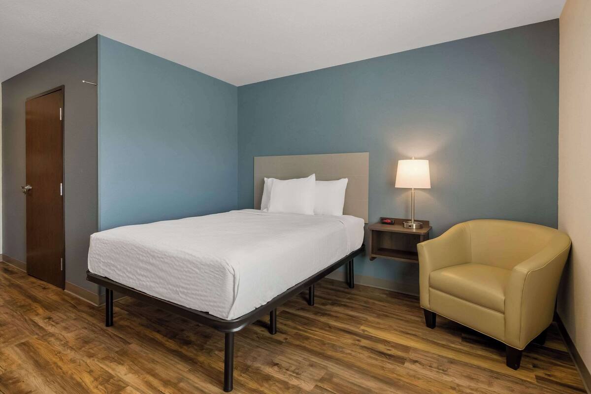 Una habitación de hotel con una cama individual, una silla, una mesita de noche y una lámpara.