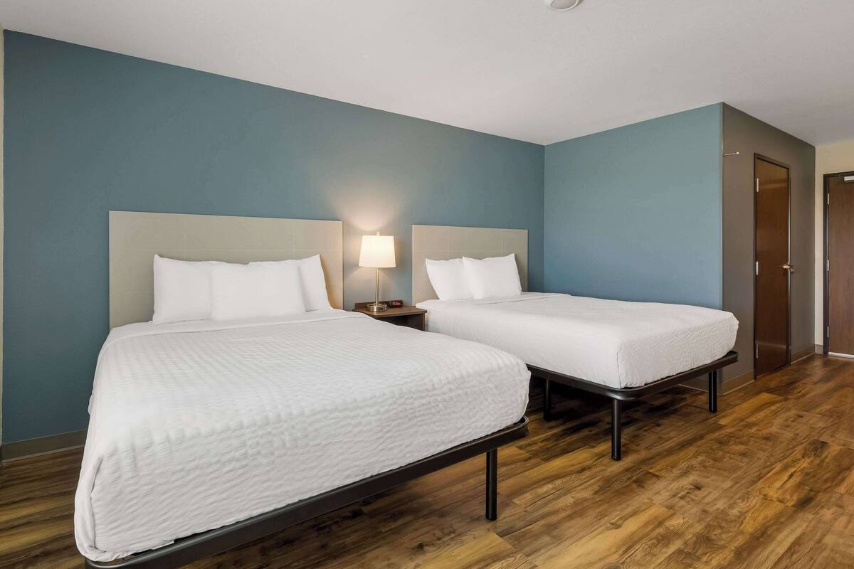 Una habitación de hotel con dos camas, una mesita de noche con lámpara y suelo de madera.