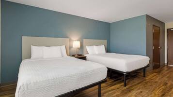 A hotel room with two beds, a nightstand with a lamp, and a wooden floor.