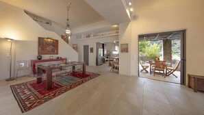 A spacious living area with a dining table, chairs, a red rug, and a kitchen in the background. - Crystal View Villa by Unique Villas Collection (Corinth)