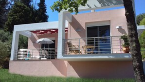 A two-story building with a balcony, a striped umbrella, and outdoor furniture. - Wohlfühloase Inmitten Alter Oliven- und Zypressenbäumen (Karousades)