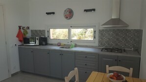 A modern kitchen with grey cabinets, a window with a view, a microwave, and a gas stove. - Wohlfühloase Inmitten Alter Oliven- und Zypressenbäumen (Karousades)