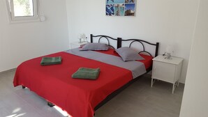 A neatly made bed with red and grey bedding, two green towels, and a nightstand with a lamp. - Wohlfühloase Inmitten Alter Oliven- und Zypressenbäumen (Karousades)