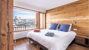 A bedroom with a wooden headboard, a large window with a mountain view, a bed with white bedding and two pillows, and a bedside table with a lamp. - Courchevel 1850, elegant, 3 bedrooms, 92sqm, ski in ski out, exceptional view (Courchevel)