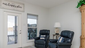 A living room with two black leather chairs, a wooden cabinet, and a sign that reads "THIS IS our happy place". - Waterfront Townhome | Boat Dock & Fish Cleaning Station (Corpus Christi)