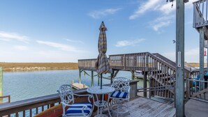 Une terrasse en bois avec une table et des chaises, donnant sur une étendue d’eau.