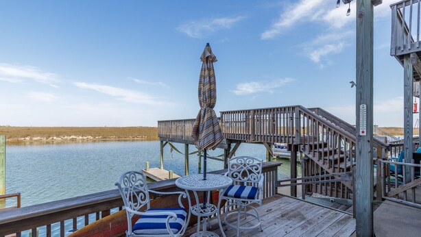 A wooden deck with a table and chairs, overlooking a body of water. - Waterfront Townhome | Boat Dock & Fish Cleaning Station (Corpus Christi)