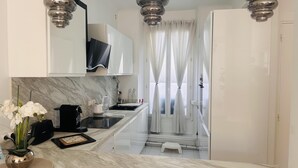 A modern kitchen with white cabinets, a marble countertop, a black coffee machine, and a small stool.