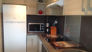 A compact kitchen with a refrigerator, microwave, coffee maker, and a cutting board. - Spacious studio in the center of Cannes, nice terrace, easy walk to the Croisette and Palais - 1923 (Cannes)