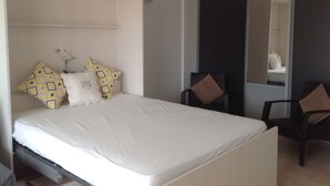 A bedroom with a bed, pillows, a chair, and a mirror. - Spacious studio in the center of Cannes, nice terrace, easy walk to the Croisette and Palais - 1923 (Cannes)