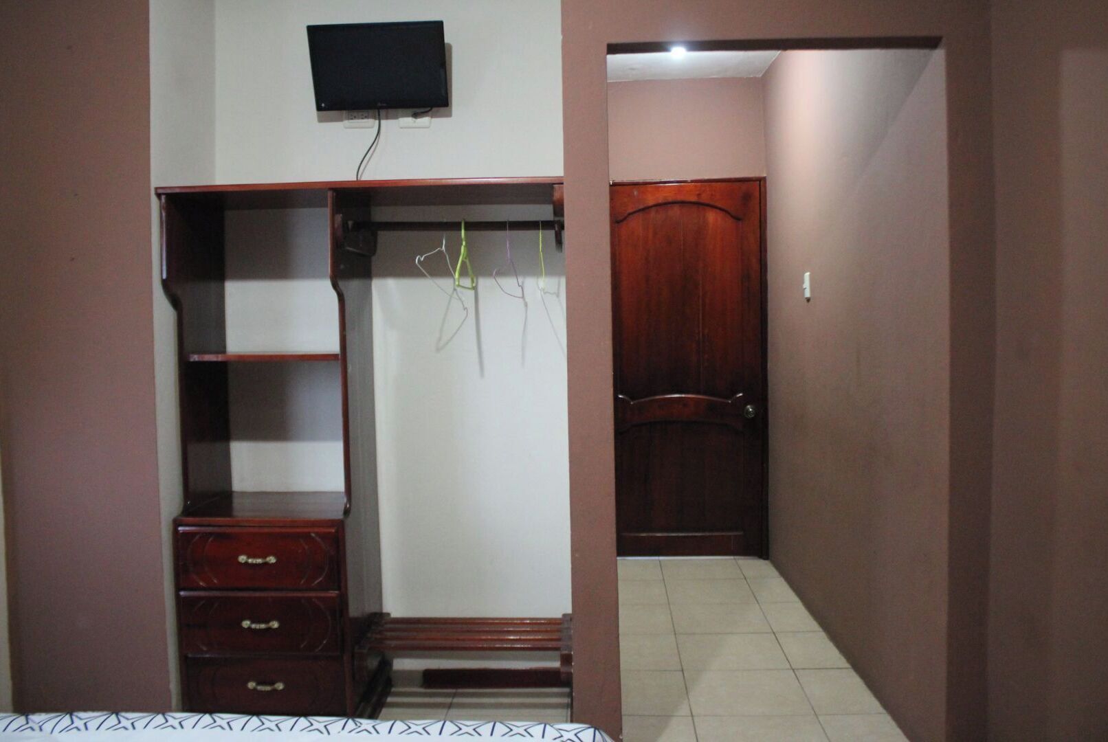 Un vestidor con estantes, cajones y espacio para colgar ropa, una puerta de madera y un televisor montado en la pared.