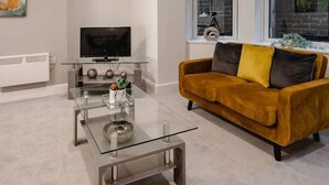 Un salon moderne avec une table basse en verre, un canapé avec des coussins, un téléviseur à écran plat et une fenêtre donnant sur un vélo et un mur de briques.