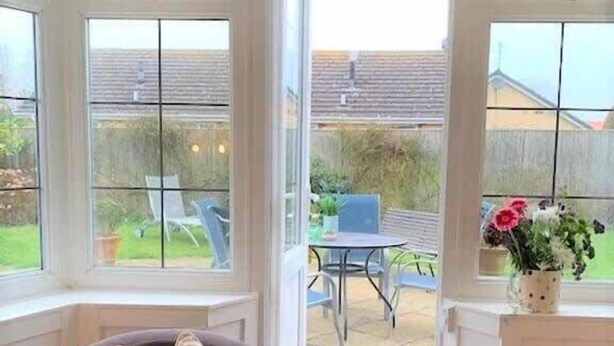 A room with a view of a patio area, including a table and chairs, and a window with a cushion on a chair. - The Garden Apartment - (Filey)