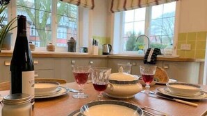 A dining table set with plates, glasses, a bottle, and a teapot, with a window in the background. - The Garden Apartment - (Filey)
