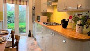 A modern kitchen with a dining area, featuring a gas stove, microwave, and cabinets. - The Garden Apartment - (Filey)