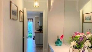 A hallway leading to a kitchen with a rug, a vase with flowers, and framed pictures on the wall. - The Garden Apartment - (Filey)