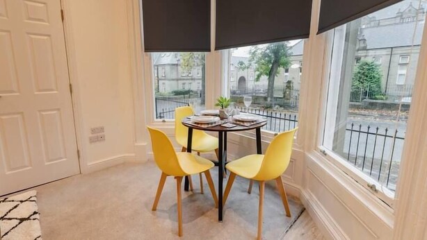 A corner room with a round table, four yellow chairs, and large windows with black blinds. - Apt 3 Prescott Court Halifax (Halifax)