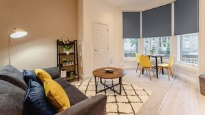 A modern living room with a grey sofa, yellow cushions, a round coffee table, and a bookshelf. - Apt 3 Prescott Court Halifax (Halifax)