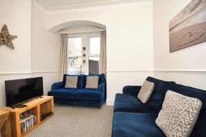 Ein Wohnzimmer mit einem blauen Sofa, einem Fernseher auf einem Holzgestell und einer Stern-Dekoration an der Wand.