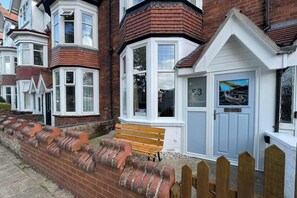 A residential building with a bay window, a door with a number, and a bench outside.