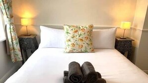 A neatly made bed with white linens, a floral pillow, and rolled towels on the bed. There are two bedside tables with lamps and a curtain on the left side. - Jackson Landing  - Spacious house with central location (Filey)