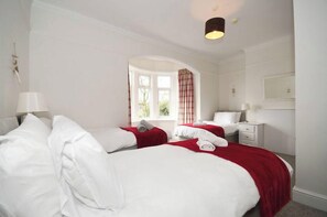 Een hotelkamer met twee bedden, een raam met gordijnen, een nachtkastje met een lamp en een spiegel aan de muur.