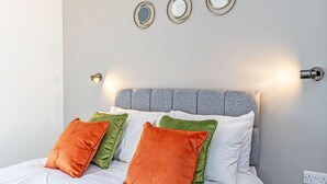 A neatly made bed with white and orange pillows, a grey headboard, and three wall-mounted mirrors. - Apt 8 Prescott Court Halifax (Halifax)