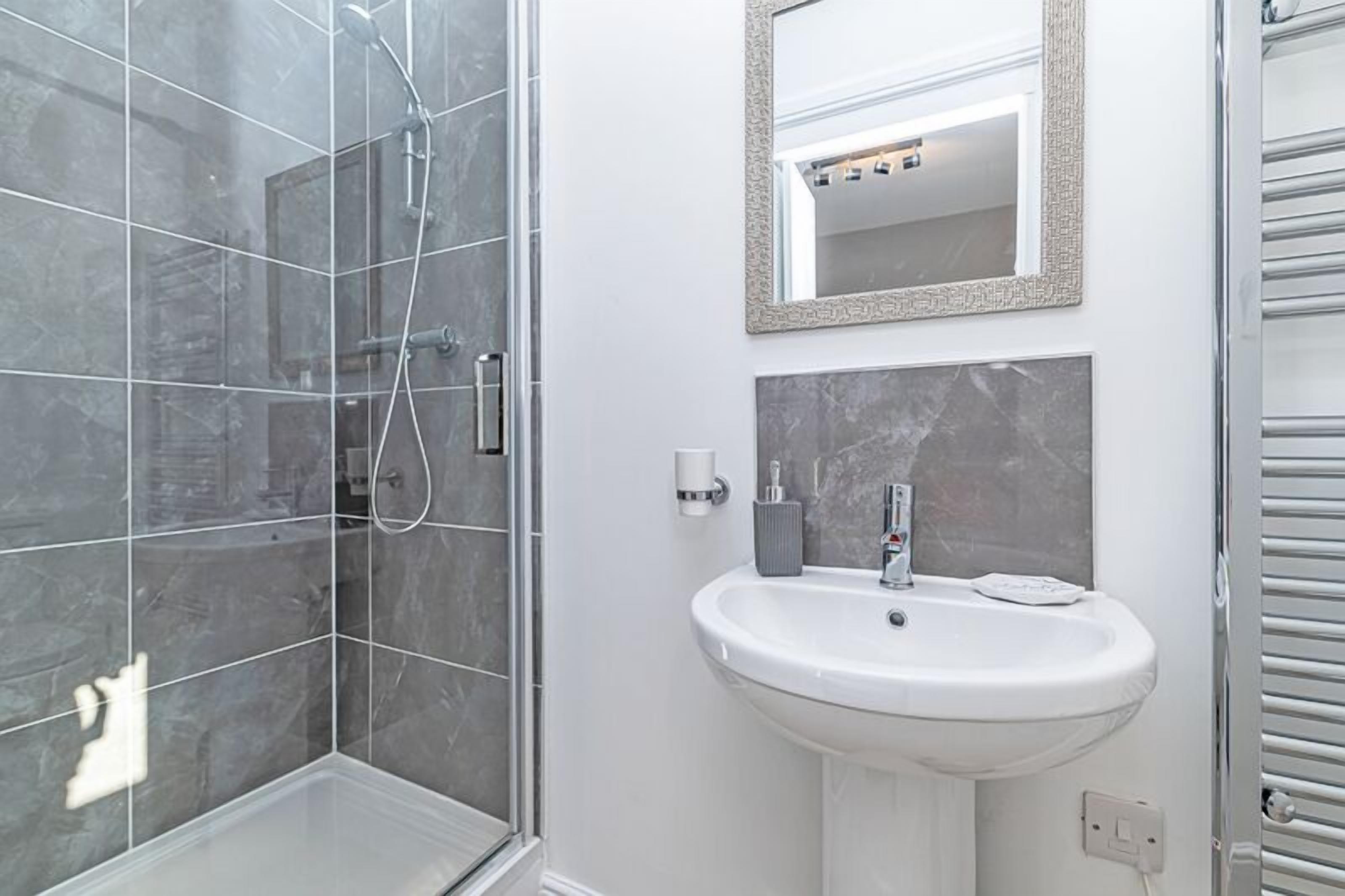 Baño con ducha, lavamanos y espejo.