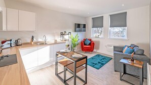 A modern kitchen with white cabinets, a dining table, and a red chair. - Apt 8 Prescott Court Halifax (Halifax)