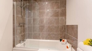 Une salle de bain moderne avec une douche à l’italienne, une baignoire blanche et une serviette ornée d’une fleur sur le côté.