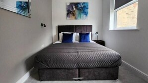 Une chambre à coucher avec un lit, une table de chevet, une fenêtre et un tableau accroché au mur.