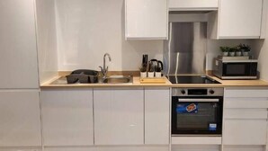 Une cuisine moderne avec des meubles blancs, un évier en acier inoxydable, un four à micro-ondes et un four traditionnel.