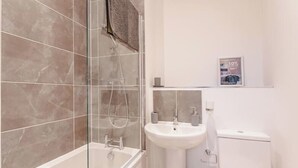 Et moderne badeværelse med en glasafskærmet bruseniche, en hvid vask og toilet.