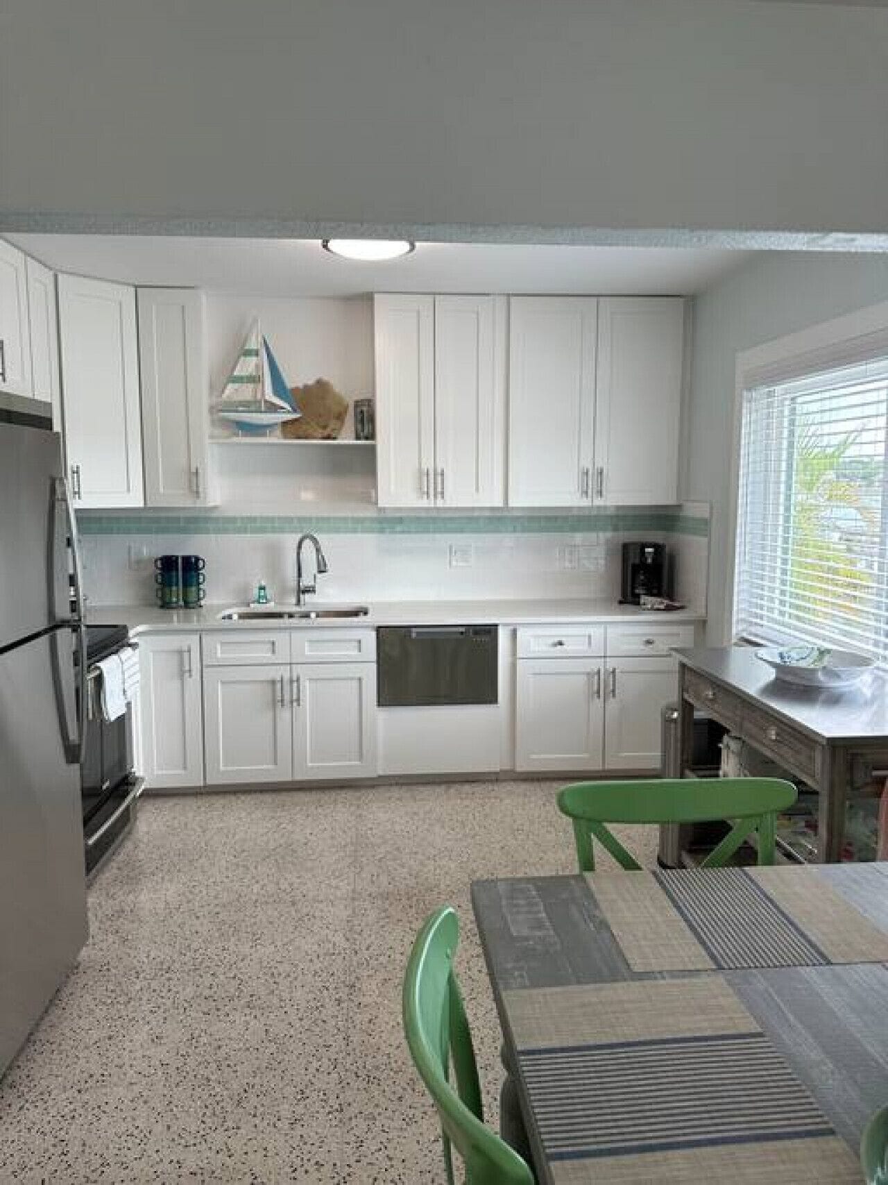 A compact kitchen with white cabinets, a stainless steel sink, and a window with blinds.