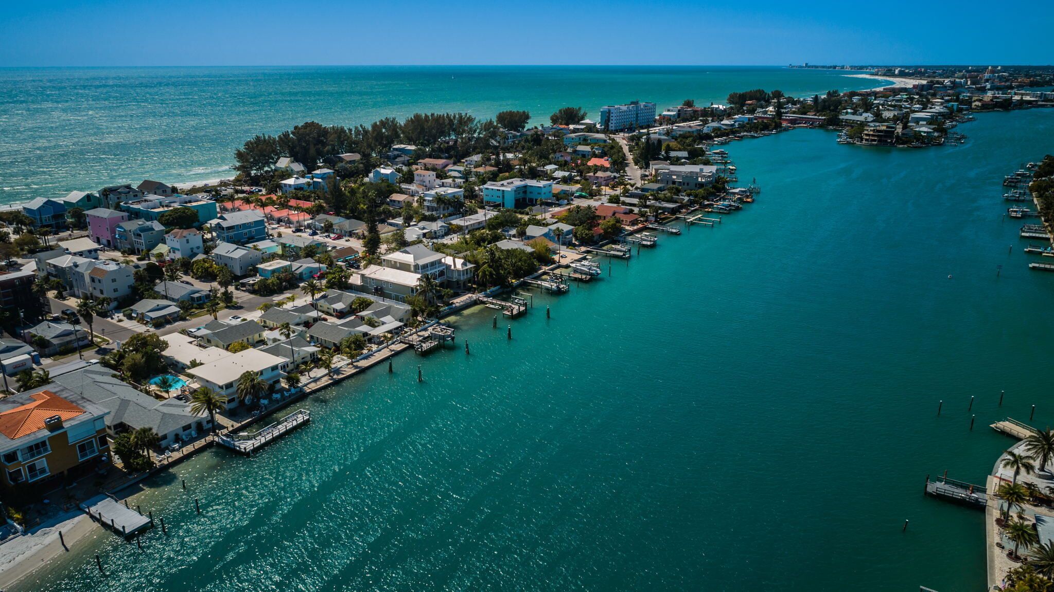 Vista aérea de un pueblo costero con un puerto deportivo, edificios residenciales y un cielo azul despejado.