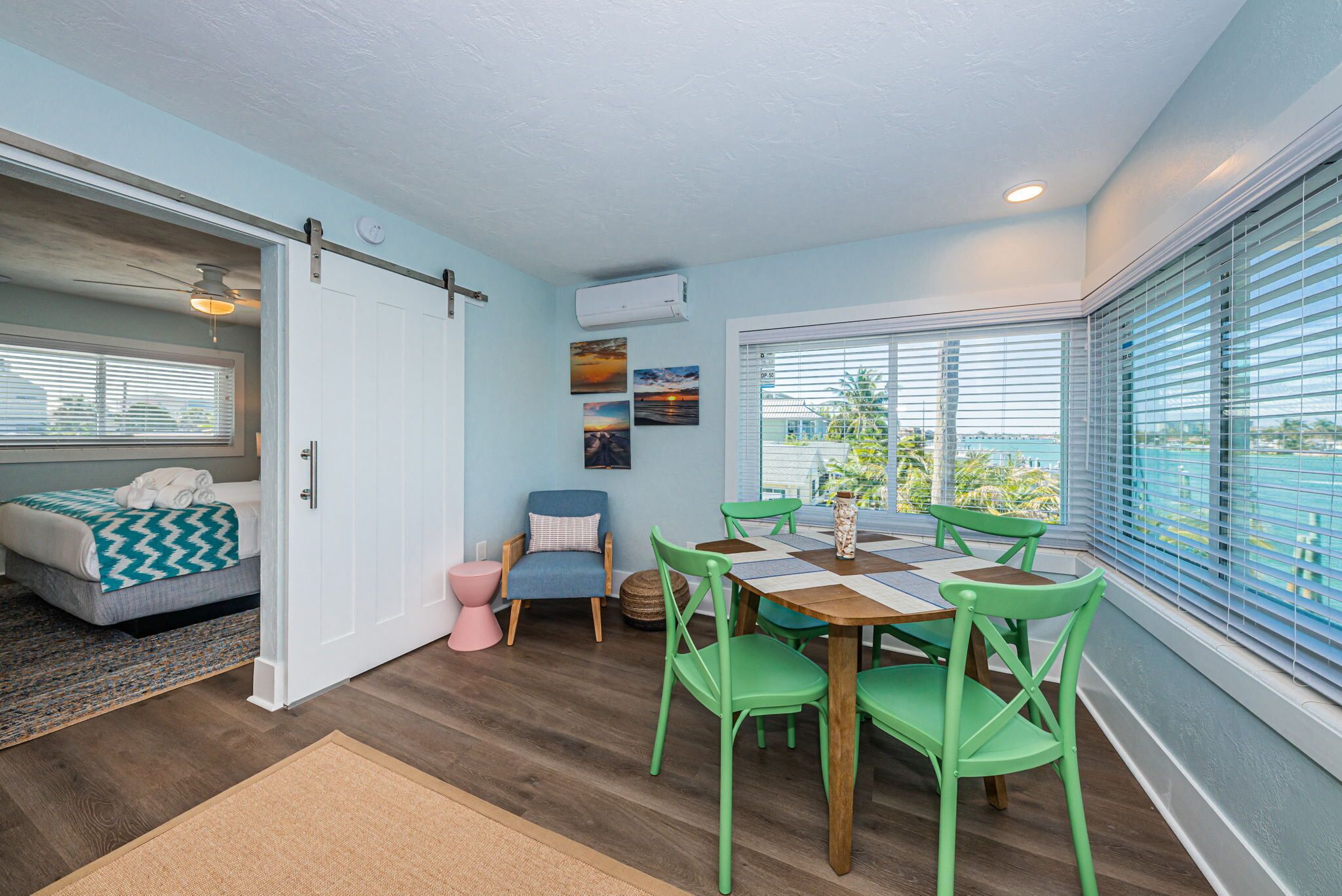 A room with a bed, a dining table with chairs, a small seating area with a chair, and a window with blinds.