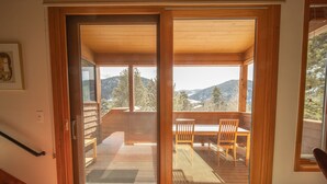 Une porte coulissante en bois donne sur une terrasse extérieure équipée d’une table et de chaises, et offre une vue sur un paysage montagneux.