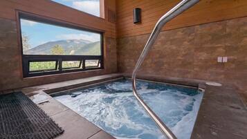 A hot tub with a view of mountains, wooden walls, and a window.