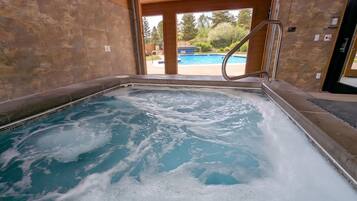 A hot tub with a view of a swimming pool and trees.
