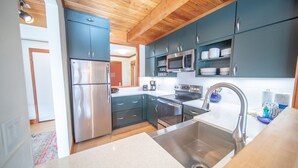 Une cuisine moderne dotée d’appareils électroménagers en acier inoxydable, de meubles de couleur bleu foncé et d’un plafond en bois.