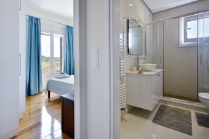A modern hotel room with a bed, a bathroom with a shower, and a view of the city. - Luxury Bay View by Corfuescapes (Corfu)