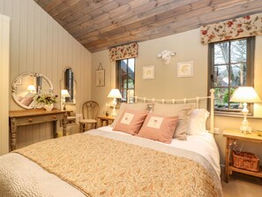 Un dormitorio con techo de madera, una cama con ropa de cama estampada, un espejo y una ventana con cortinas florales.
