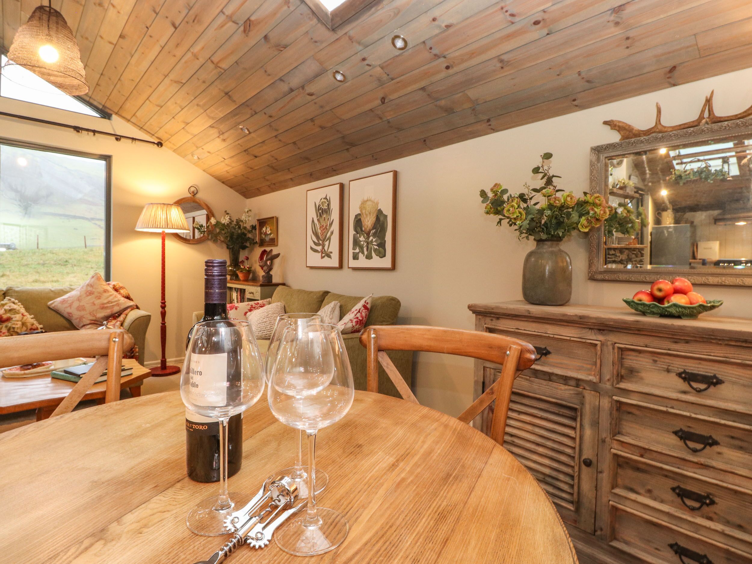 A wooden dining table with wine bottles and glasses, a wooden chair, and a cabinet with drawers.