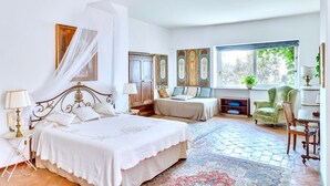 A spacious bedroom with a large bed, a sitting area with a chair, a small table, and a window with a view of trees. - VILLA OASI - Four Bedroom Villa, Sleeps 8 (Positano)