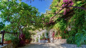 A stone-paved courtyard with a pergola covered in flowering vines, surrounded by lush greenery and potted plants. - VILLA OASI - Four Bedroom Villa, Sleeps 8 (Positano)