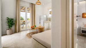 Camera d'albergo moderna con un letto, un'area pranzo con tavolo e sedie, un frigorifero e un'ampia finestra con tende.