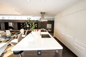 Een moderne keuken met een centraal eiland, witte kasten en een eetgedeelte met witte stoelen.