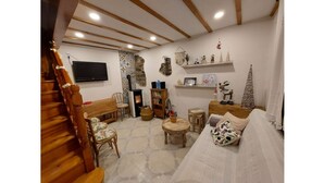Una sala de estar acogedora con una escalera de madera, un sofá, un televisor y varios objetos decorativos en las paredes.