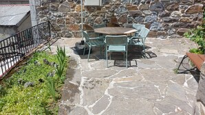 Un patio exterior con suelo de piedra, una mesa con sillas y un paraguas blanco.