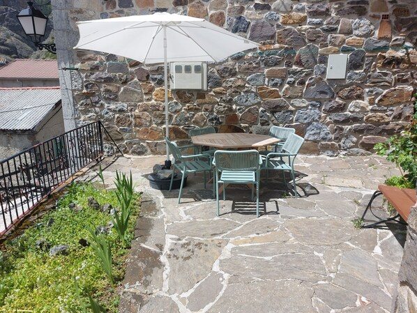 Un patio exterior con suelo de piedra, una mesa con sillas y un paraguas blanco.